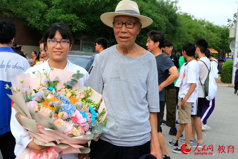 老爺爺早早來到考點前等候,第一時間為孫女送上一大束鮮花。李依環 攝