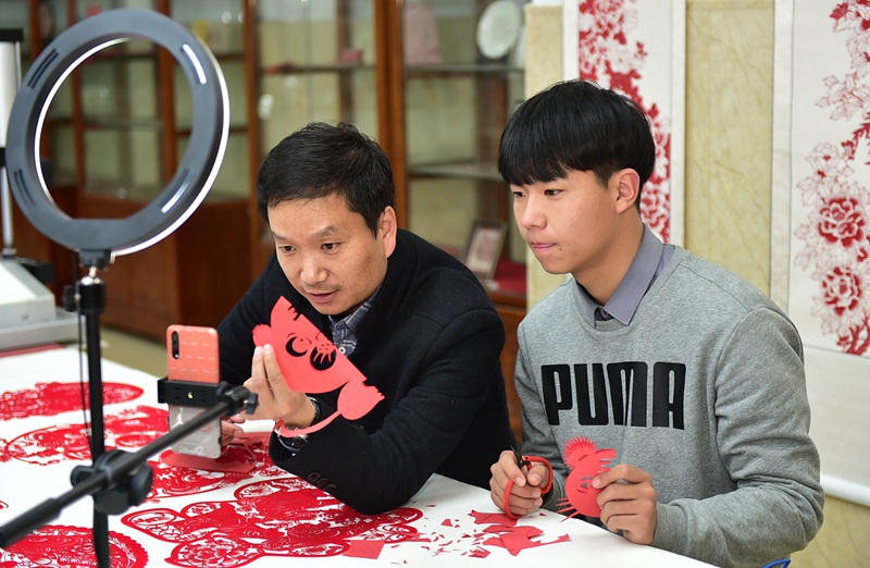 河南省省級非遺項目剪紙技藝代表性傳承人王飛(左)與學員，通過“雲端”向大家展示剪紙技藝。 黃政偉攝 
