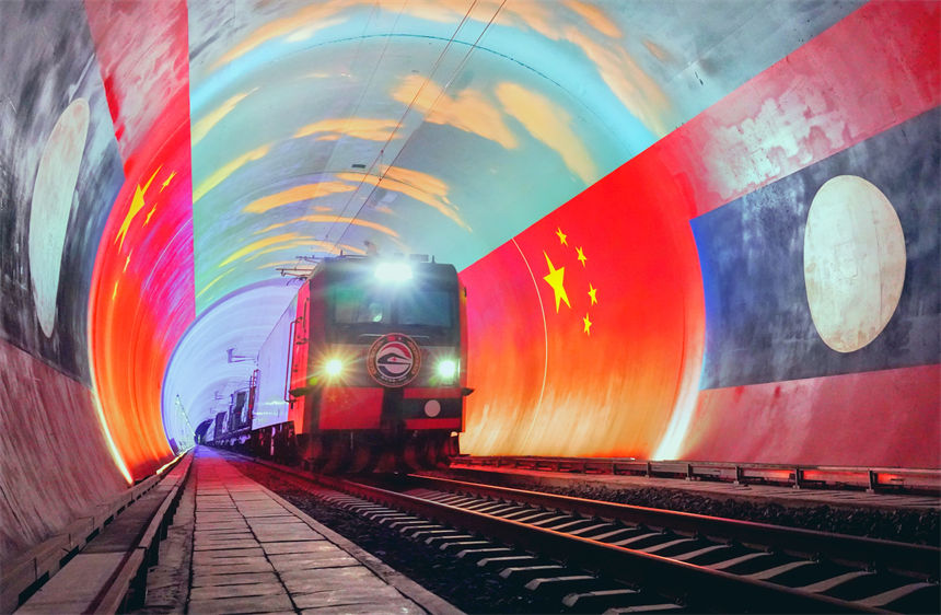 在中国和老挝两国国旗映衬下，卫生列车即将在中老铁路“友谊隧道”内跨越中老两国边境。凯乔摄