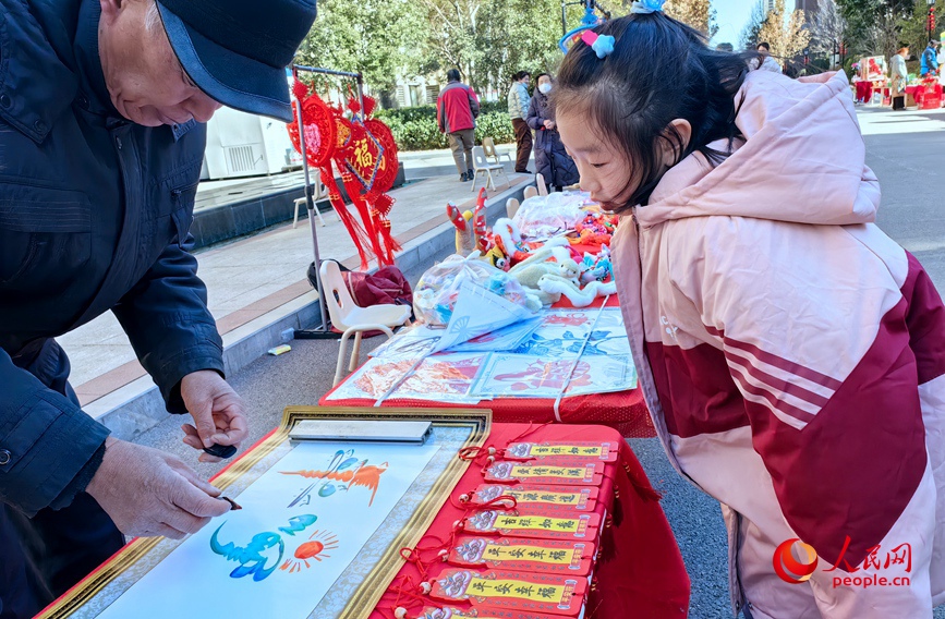 民間花鳥字傳承人高景文正在創作“平安幸福”，吸引了小朋友駐足觀看。人民網 侯琳琳攝