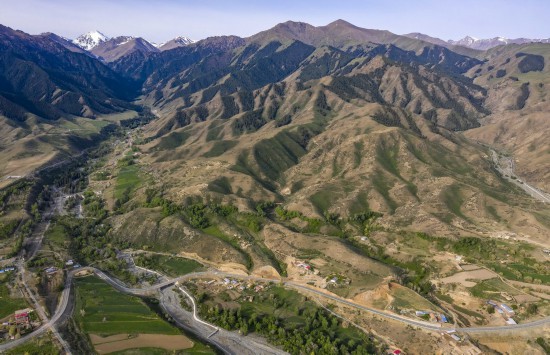 新疆吉木萨尔县新地乡的一处伴山乡间公路（2022年5月22日摄，无人机照片）。路旁的小分子村发展乡村旅游，成为远近闻名的“画家村”。新华社记者 胡虎虎 摄